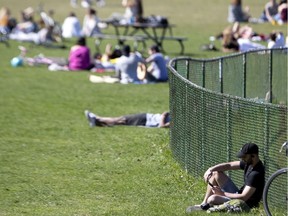 A man reads alone, away from others in a busy Jeanne-Mance Park as the city deals with the coronavirus pandemic in Montreal, on Monday, May 18, 2020. While those in the background might be adhering to the rules (it can be hard to know which park visitors are members of the same household), Fariha Naqvi-Mohamed says she is aware of gatherings at people's homes that have violated the 10-person maximum.