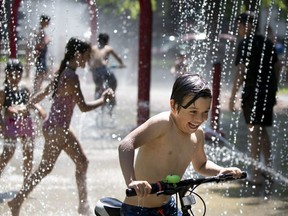 Nathaniel Verzamanis is delighted as he rides his bike through the splash pad installations at Parc de Lestre during an early heat wave in Montreal, on Wednesday, May 27, 2020.