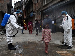 Health workers wearing protective suits spray disinfectant on a young girl during a government-imposed nationwide lockdown as a preventive measure against the COVID-19 coronavirus on a deserted road in Kathmandu on Sunday, May 3, 2020.