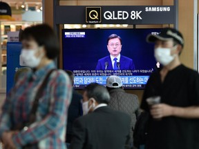 People wearing face masks watch a television news broadcast showing a speech of South Korean President Moon Jae-in on the occasion of the third anniversary of his inauguration, at a railway station in Seoul on May 10, 2020. - South Korea's capital has ordered the closure of all clubs and bars after a burst of new cases sparked fears of a second coronavirus wave as President Moon Jae-in urged the public to remain vigilant. (Photo by Jung Yeon-je / AFP)