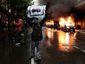 A man holds an image of a fist in front of burning vehicles following demonstrations protesting the death of George Floyd, a black man who died May 25 in the custody of Minneapolis Police, in Seattle, Washington on Saturday, May 30, 2020.