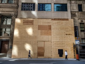 Pedestrians walk past and stand in front a shuttered business on Bay Street in Toronto in April.