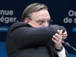 Quebec Premier François Legault coughs in his sleeve during Thursday's news conference in Montreal.