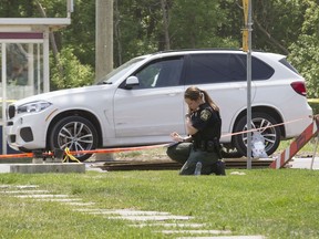 A Laval police officer takes notes at the scene of a fatal shooting on May 27, 2016, in which 67-year-old Rocco Sollecito, a Montreal Mafia leader, was killed. Police believe the suspect waited in the bus shed for Sollecito, who was driving the white BMW SUV, to arrive.
