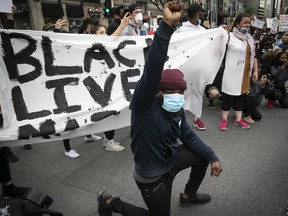Protester raises his fist and puts a knee to the ground during anti-racism and anti-police-brutality demonstration on Sunday May 31, 2020. Most protesters wore masks.