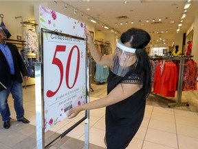 Saleswoman Nelly Kara installs a sale sign at the entrance to the Manteaux Manteau store in Fairview Pointe Claire shopping mall, west of Montreal Friday June 19, 2020.