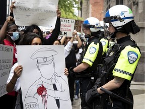 A line of SPVM police officers dressed in crowd control gear look on as protesters show them signs and chat at them during an anti police brutality march in Montreal, on Sunday, June 7, 2020.