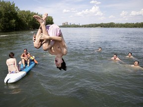 Ethan Caldwell does a flip as he dives in the St. Lawrence River to join his friends as Maryse, left, and Anne-Sophie watch from their paddle board during as heat wave in Verdun June 22, 2020.