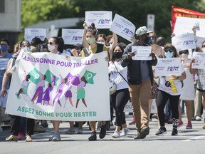 People hold up signs during a demonstration outside Prime Minister Justin Trudeau's constituency office in Montreal, Saturday, June 6, 2020, where they called on the government to give residency status to migrant workers as the COVID-19 pandemic continues in Canada and around the world.