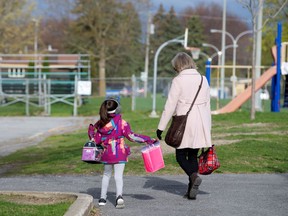A student is escorted into the schoolyard by a teacher in St-Jean-sur-Richelieu as schools outside the greater Montreal region began reopening on May 11, 2020.
