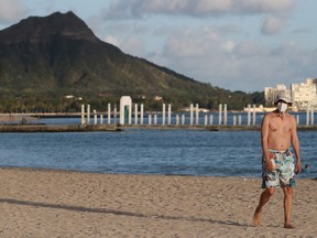 A beachgoer wearing a protective mask walks down Waikiki Beach, with Diamond Head mountain in the background, during the spread of the coronavirus disease (COVID-19) in Honolulu on April 28, 2020.