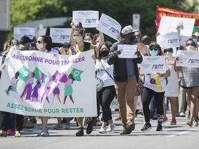 People hold up signs during a demonstration outside Prime Minister Justin Trudeau's constituency office in Montreal, Saturday, June 6, 2020, where they called on the government to give residency status to migrant workers as the COVID-19 pandemic continues in Canada and around the world.