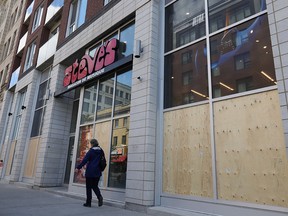 A pedestrian walks by the boarded-up Steve’s Music store on Ste-Catherine St. in Montreal June 1, 2020, after the windows were smashed by looters after a peaceful anti-racism demonstration Sunday night.