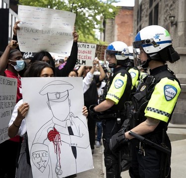 A line of SPVM police officers dressed in crowd control gear look on as protesters show them signs and chat at them during march against racism and police brutality in Montreal on Sunday, June 7, 2020.