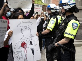 A line of SPVM police officers dressed in crowd control gear look on as protesters show them signs and chat at them during march against racism and police brutality in Montreal on Sunday, June 7, 2020.