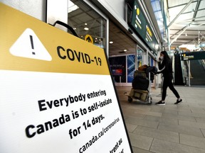 A traveler walks past signage asking international travellers to self-isolate for 14 days in Vancouver International Airport.