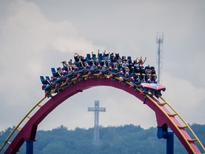 The Mount-Royal cross is seen in the background as people ride the Goliath rollercoaster at the La Ronde amusement park in Montreal on Thursday, June 11, 2015.