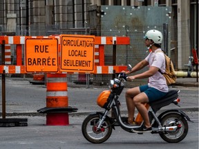 A scooter rider passes by orange construction cones and redirection signs at Saint-Pierre Street and Marguerite D'Youville Street in Montreal on Friday June 26, 2020.  Dave Sidaway / Montreal Gazette