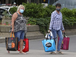 A couple of women  wearing masks carry shopping bags across Atwater Ave. in Montreal Tuesday June 30, 2020.