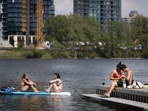 Anne-Sophie, left, and Maryse relax on their paddle board as Maxime Dursin and Nadia Saadoune sit on a wharf on the St. Lawrence River during a heat wave in Montreal on June 22.