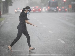 A woman wearing mask and face shield runs across Rene-Levesque Blvd. to get away from early afternoon rain in July 2020.