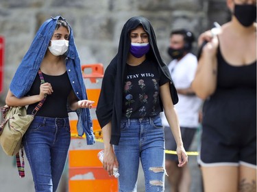 Two women use shirts on their heads to shield themselves from the sun as they wait in line for COVID-19 testing at the former Hôtel-Dieu hospital in Montreal Wednesday July 15, 2020.
