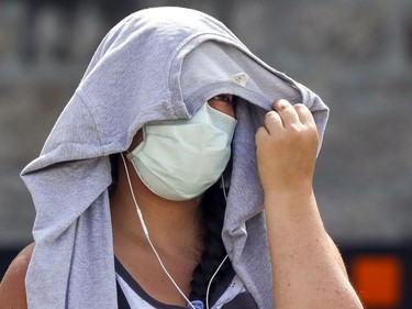 A woman uses a sweatshirt on her head to shield herself from the sun as she waits in line for COVID-19 testing at the former Hôtel-Dieu hospital in Montreal Wednesday July 15, 2020.