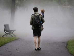 David Dionise carries his son, Henri, into the mist in Montreal, on Friday, July 17, 2020. (Allen McInnis / MONTREAL GAZETTE)
