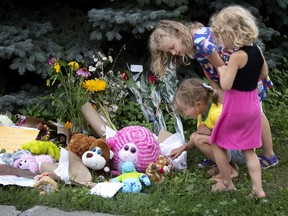 Romi Shank-Menard, kneeling, Kalya Fisico, rear, and Cynthia Shank-Menard look at the flowers and notes left for an 8-year-old boy who was hit and killed by a car outside a day camp in St-Henri on Wednesday.