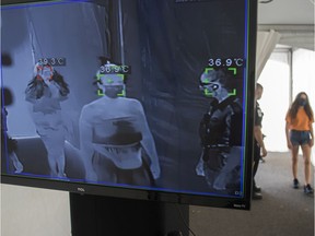 Masked people have their temperature taken by a thermal imaging camera as they enter La Ronde in Montreal on Saturday, July 25, 2020.