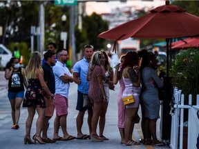 People stand in queue to enter a restaurant on Ocean Drive in Miami Beach, Florida on June 26, 2020. - They are itching for a good time after months of lockdown, and may the coronavirus be damned: young adults in Florida are fueling a dangerous rise in COVID-19 infections. Feeling immortal, these fun-crazed people are finding ways to gather and party even though many bars and nightclubs remain closed as the Sunshine State reopened its economy this month. (Photo by CHANDAN KHANNA / AFP)
