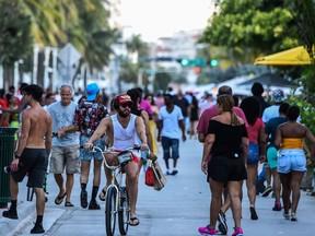 A man rides a bicycle as people walk on Ocean Drive in Miami Beach on June 26, 2020. Florida has registered more than 15,000 new cases of coronavirus in a day, easily breaking a record for a U.S. state previously held by California, according to official numbers published on July 12, 2020. The total of 15,299 cases in the hard-hit southeastern state was up sharply, 47 per cent above the previous day's total, the Florida state health department reported.