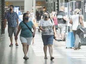 People wear face masks as they walk through a shopping mall in Montreal on Saturday, July 18, 2020. The wearing of masks or protective face coverings became mandatory in Quebec as of Saturday.