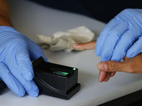 A German federal police officer takes digital fingerprints of a refugee who arrived without documents in Rosenheim, Germany, Tuesday, July 28, 2015. The government has quietly relaxed a requirement to fingerprint prospective new federal hires as part of security screening, a move prompted by the need for physical distancing during the pandemic.