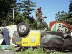 A Mohawk Warrior stands atop overturned police vehicles Wednesday, July 11, 1990 the morning of the start of the Oka Crisis in Kanesatake near Montreal.