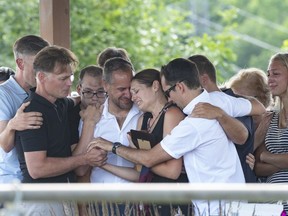 Amelie Lemieux, centre, is comforted by family members as she holds pictures of her two daughters, Romy and Norah Carpentier, at a memorial in Lévis on Monday, July 13, 2020. The bodies of Norah and Romy Carpentier, aged 11 and 6, were located in a wooded area in St-Apollinaire, but Martin Carpentier, who is suspected of abducting the girls, remains missing.