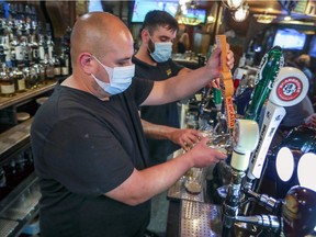 Manager Carlos Bustamante, left, draws a pint of beer behind the bar at McKibbin's Irish Pub in Montreal on Saturday, Aug. 8, 2020.