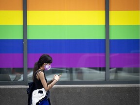 A woman in a colourful, washable, protective face mask walks past a window decorated in the colours of the rainbow in Montreal, on Friday, August 21, 2020.