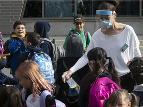 Teacher Saba Ghaffari, wearing visor and mask, sprays disinfectant on the hands of students as they line up for class in schoolyard at Philippe-Labarre, during back to school day at the CSDM in Montreal on Thursday August 27, 2020.