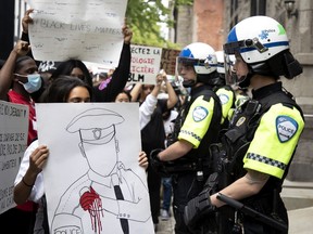 A line of Montreal police officers dressed in crowd-control gear look on as protesters show them signs during an anti-police brutality march in Montreal on June 7, 2020.