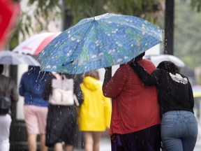 A mom and her daughter try, somewhat unsuccessfully to huddle under one umbrella as they walk in the rain along Sainte-Catherine Street in Montreal, on Sunday, August 2, 2020. (Allen McInnis / MONTREAL GAZETTE)