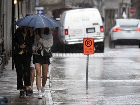 Two pedestrians huddle under one umbrella as St-Paul Street begins to pool with water during a day of steady rain fall in Montreal, on Tuesday, Aug. 4, 2020.