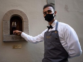 A waiter puts a glass of wine in the "buchetta del vino" a small window to serve wine, a tradition which exists since the Renaissance period and that is typical in the streets of Florence, on August 12, 2020.