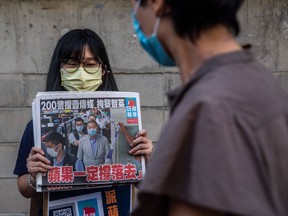 A volunteer poses holding a copy of the Apple Daily newspaper - paid for by a collection of pro-democracy district councillors - before handing them out in Hong Kong on August 11, 2020, a day after authorities conducted a search of the newspaper's headquarters after the companys founder Jimmy Lai was arrested under the new national security law. - Hong Kong pro-democracy media tycoon Jimmy Lai was arrested on August 10 and led in handcuffs through his newspaper office as police raided the building, part of a sweeping crackdown on dissent since China imposed a security law on the city. (Photo by ISAAC LAWRENCE / AFP)