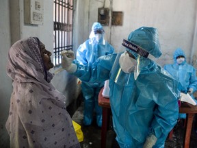 A health worker (R) wearing a Personal Protective Equipment (PPE) suit collects a swab sample from a woman for Rapid Antigen Test (RAT) for the Covid-19 coronavirus at a testing centre in Siliguri on August 29, 2020. (Photo by DIPTENDU DUTTA / AFP)