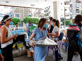 Volunteers, clad in masks due to the COVID-19 coronavirus pandemic, walk with trays of meals to be distributed upon people affected by the Beirut port explosion in the Ashrafieh neighbourhood of Lebanon's capital Beirut on August 10, 2020.