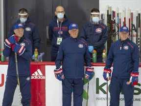 Montreal Canadiens head coach Claude Julien, centre, flanked by assistant coaches Kirk Muller, left, and Domenic Ducharme, right, keep an eye on practice as support staff wearing protective equipment look on as they hold their first team practice on July 13, 2020, in Brossard.