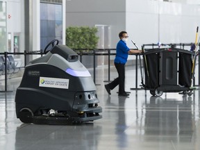 An automated floor cleaner that sanitizes the floor is shown as a worker walks by at Pearson International Airport during the COVID-19 pandemic in Toronto on June 23, 2020. Hospitality workers are calling on various levels of the government to work creatively and avoid long-term unemployment in the sector.