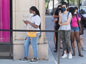 People wear face masks as they wait to enter a store in Montreal, Saturday, Aug. 8, 2020, as the COVID-19 pandemic continues in Canada and around the world.