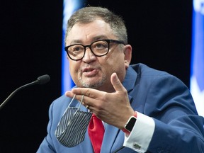 Dr. Horacio Arruda, Quebec's director of public health, holds up his face mask as he unveils an updated back-to-school plan for the 2020-2021 school year at a news conference in Montreal, Monday, Aug. 10, 2020.